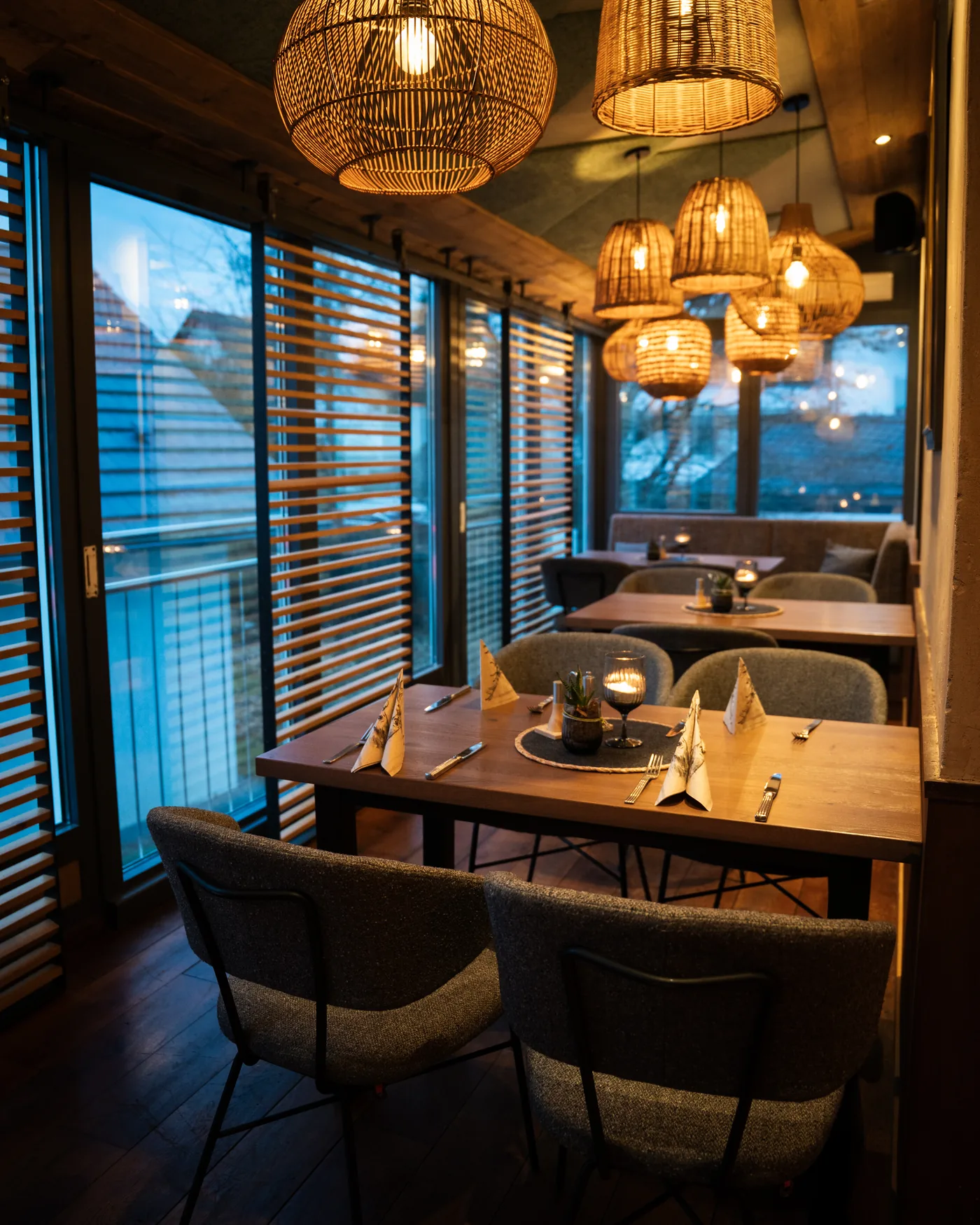 Wintergarten mit Korblampen und eingedeckten Tischen in der Abenddämmerung